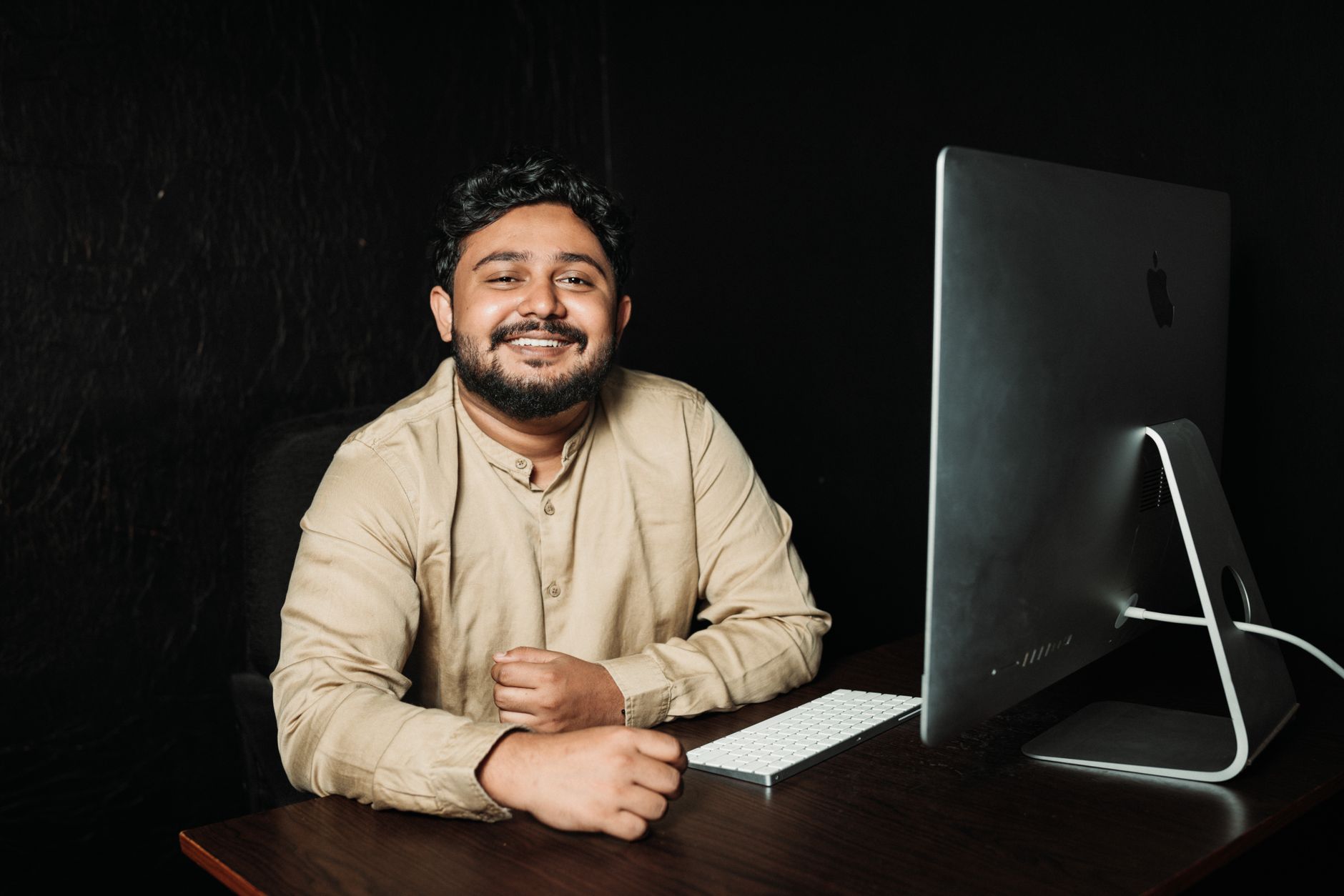 Jovem sorridente sentado à mesa a trabalhar num computador de escritório, a rever um site em construção.